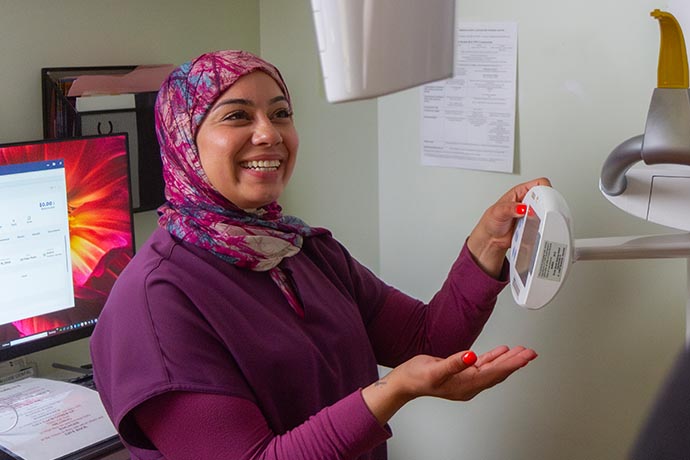 A female dental staff smiles and showcases tools inside the clinic of Allure Dental office
