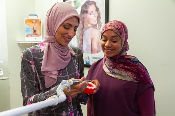 Dr. Iman Ayoubi works on a dental sample as a female patient looks on