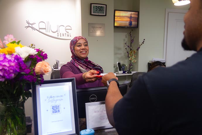 A female dental staff smiles to a male patient at the front desk