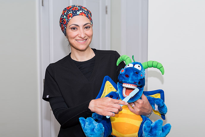 Dr. Iman Ayoubi with a stuffed toy and a large toothbrush
